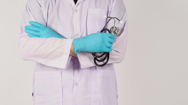 聴診器を持ったドクターハンド。手は白い背景に青い医療用手袋と長袖のガウンを着用します。
