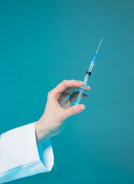 青い実験室の背景に薬やワクチンの注射器で医者の手