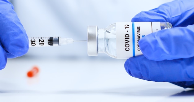 Doctor hands in blue medical gloves with transparent liquid coronavirus vaccine bottle