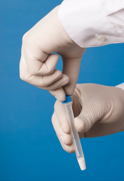 Doctor hands closing transport vial for coronavirus analysis on blue background