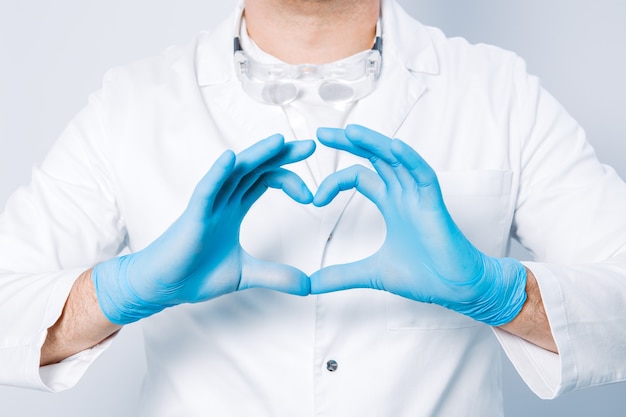 Doctor hands in gloves in the heart shape against the surface of his body and medical gown