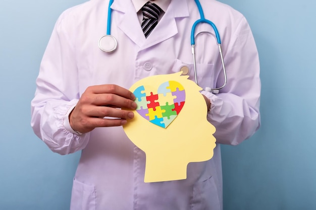 Doctor hands holding head with jigsaw puzzle heart shape. Autism spectrum disorder concept. World Autism Awareness Day.