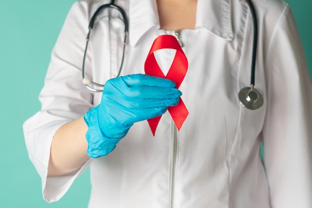 Doctor Hands is Holding Red Ribbon, AIDS, HIV International Symbol of Awareness, Healthcare and Medicine Concept. Close-Up of Female Medicine in Lab Uniform Showing Ribbon For Care HIV Symbolisms