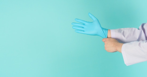 Doctor hands is pulling blue latex glove on green mint OR tiffany blue background.He wear long sleeve gown.