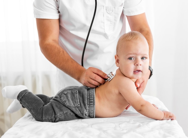 Foto mani del medico che ascoltano piccolo bambino con lo stetoscopio