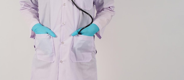 医師は聴診器でポケットに手を入れます手は白い背景に青い医療用手袋と長袖のガウンを着用します
