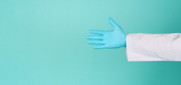 Le mani del medico indossano guanti in lattice blu su sfondo verde menta o blu tiffany. indossa un abito a maniche lunghe. mano vuota