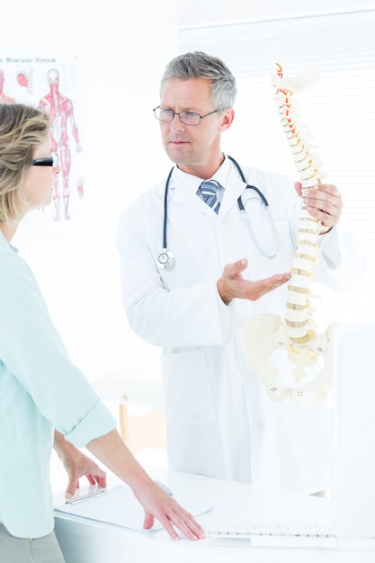 Doctor having conversation with his patient and showing spine model