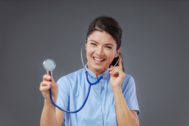 Doctor having stethoscope in ears and reaching with it towards camera like she is gonna examine.