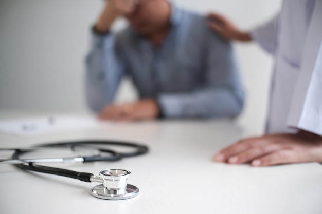 Foto medico sanitario medico professionista in abito bianco uniforme cappotto intervista consultazione paziente rassicurando il suo paziente di sesso maschile aiutando la mano