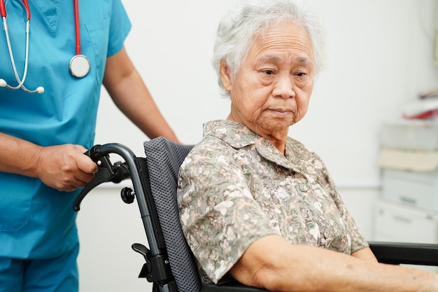 Врач помогает азиатской пожилой женщине-пациенту с инвалидностью, сидящей в инвалидной коляске в больнице.