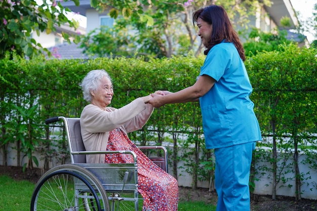 Assistenza medica paziente con disabilità della donna anziana asiatica seduto su sedia a rotelle nel concetto medico del parco