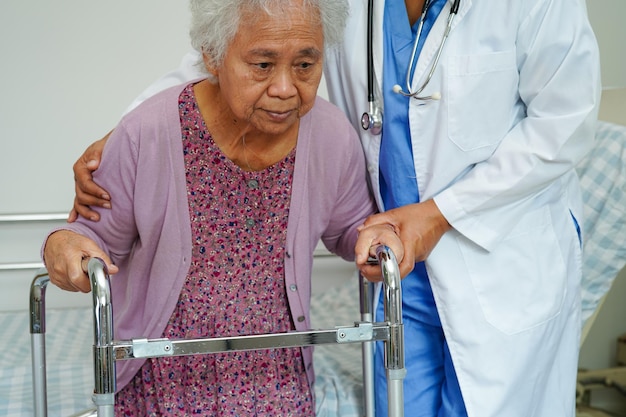 의사는 아시아 노인 여성 장애 환자가 간호 병원 의료 개념에서 워커와 함께 걷도록 도와줍니다.
