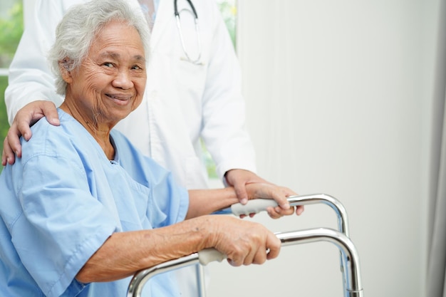 Doctor help Asian elderly woman disability patient walk with walker in nursing hospital medical concept