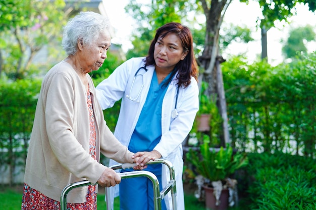 Doctor help Asian elderly woman disability patient walk with walker in park medical concept