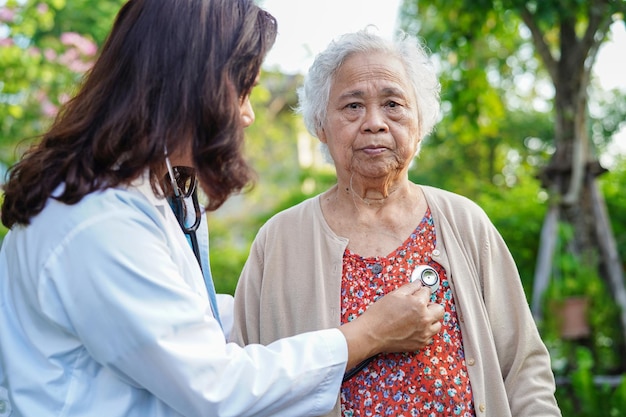 Doctor help Asian elderly woman disability patient walk with walker in park medical concept