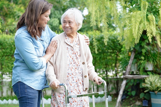 Doctor help Asian elderly woman disability patient walk with walker in park medical concept