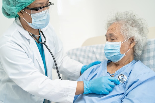 医師は、安全感染を保護し、Covid-19コロナウイルスを殺すために病院でフェイスマスクを着用しているアジアの高齢者または高齢の老婦人女性患者を助けます。