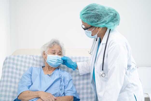 Doctor help Asian senior or elderly old lady woman patient wearing a face mask in hospital for protect safety infection and kill Covid-19 Coronavirus.