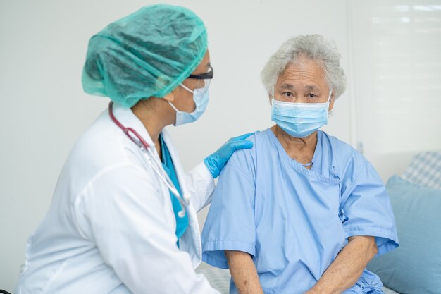 Doctor help Asian senior woman patient wearing a face mask in hospital for protect Coronavirus