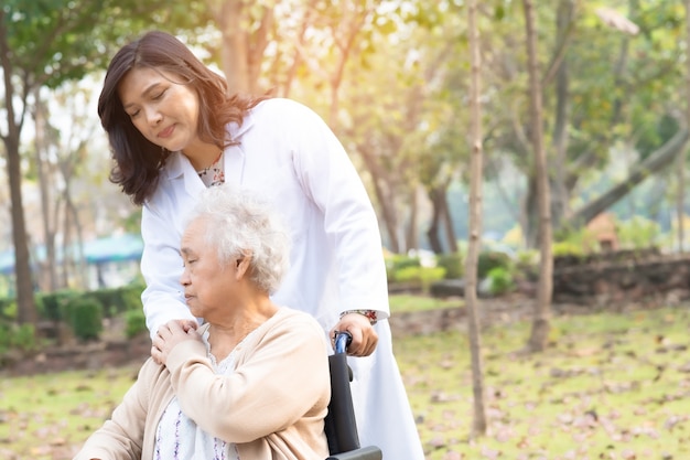 Doctor help and care Asian senior woman patient sitting on wheelchair at park.