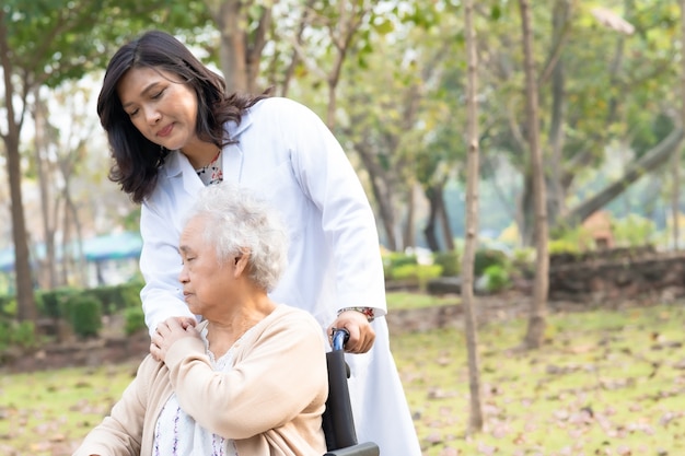 Doctor help and care Asian senior woman patient sitting on wheelchair at park.