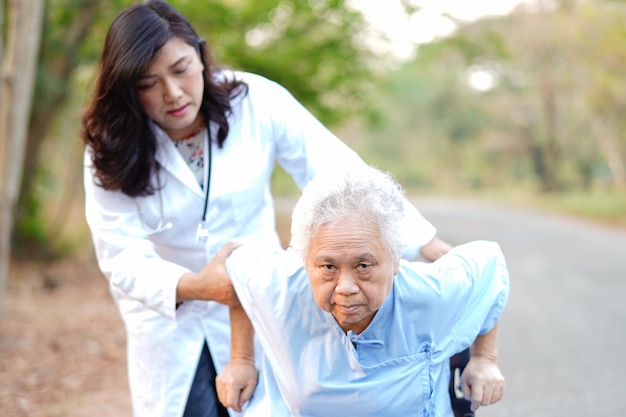 Doctor help and care Asian senior woman patient sitting on wheelchair at park.