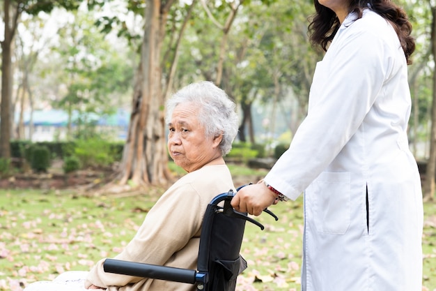 Doctor help and care Asian senior woman patient sitting on wheelchair at park.