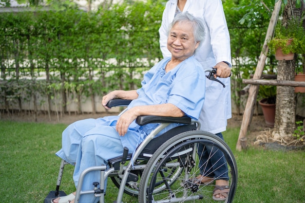 医師の助けとケア公園で車椅子に座っているアジアの年配の女性患者