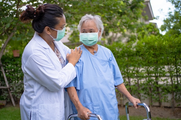 Il dottore aiuta e cura la donna anziana asiatica usa il camminatore con una buona salute mentre cammina al parco