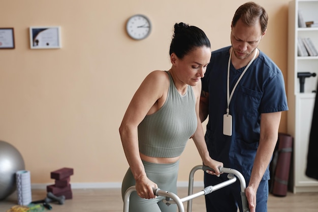 Doctor helping patient to walk using walker during rehabilitation in hospital