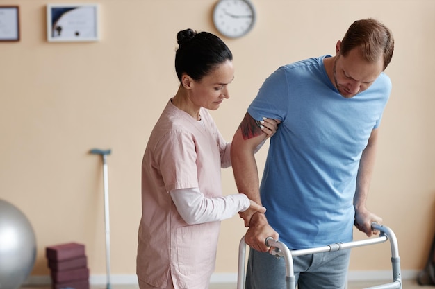 Doctor helping patient to walk with walker during his rehabilitation in hospital