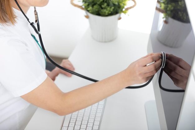 Doctor at his desk, listening with the stethoscope to the computer.