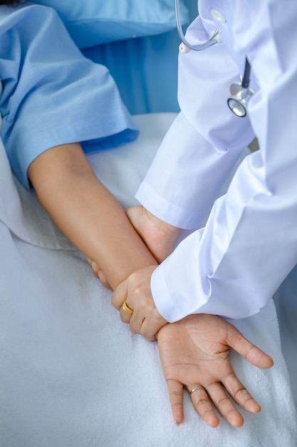 医師は病院のベッドで患者の手を握り、治療と治療のために神経系を検査します。ギランバレー症候群としびれ病またはワクチンの副作用の概念。