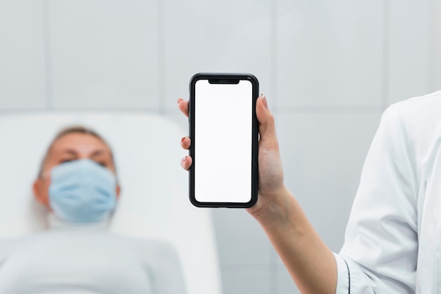 Доктор держит пустой телефон рядом с пациентом