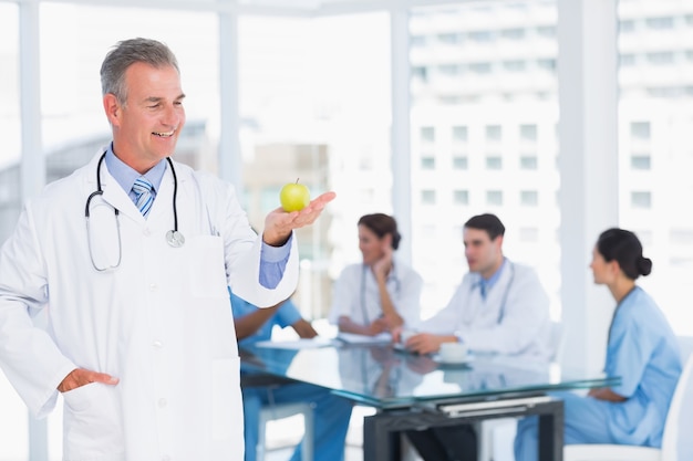 Doctor holding apple with group around table at hospital