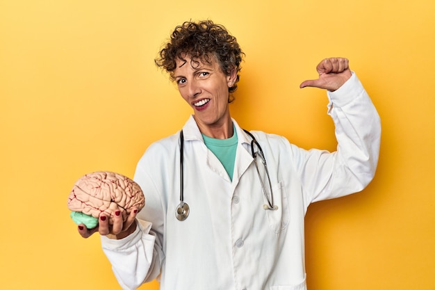 Photo doctor holding a brain model on yellow studio feels proud and self confident example to follow