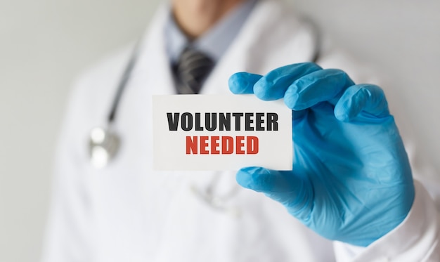 Doctor holding a card with text Volunteer Needed, medical concept