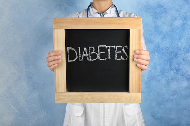 Doctor holding chalkboard with word DIABETES on color background