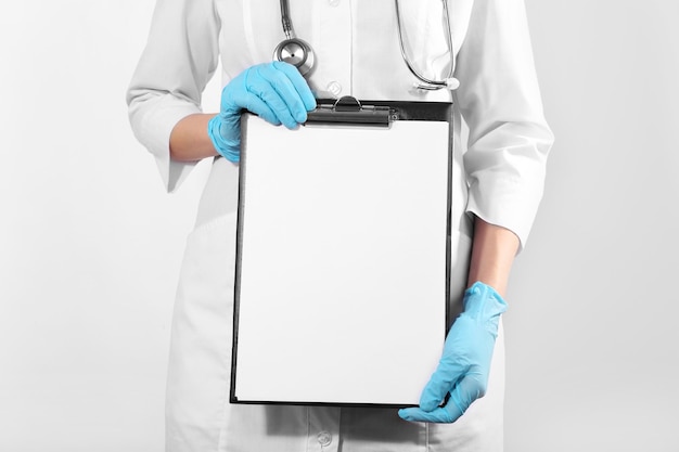 Doctor holding clipboard on light background