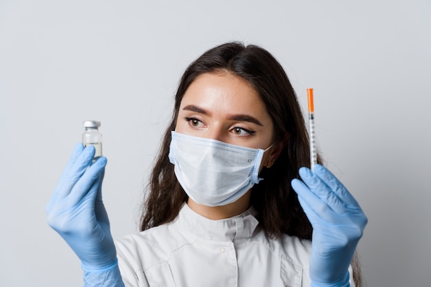 Medico che tiene il vaccino contro il coronavirus. ragazza attraente in guanti medicali con siringa e farmaci