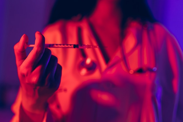 Doctor holding Coronavirus vaccine in the syringe using for prevent infection in ultraviolet neon light.