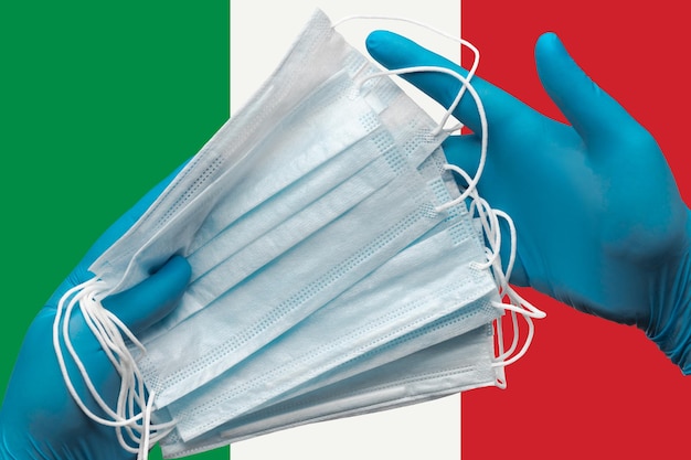 Medico che tiene le maschere per il viso nelle mani guanti blu medici su sfondo bandiera nazionale dell'italia concetto ...