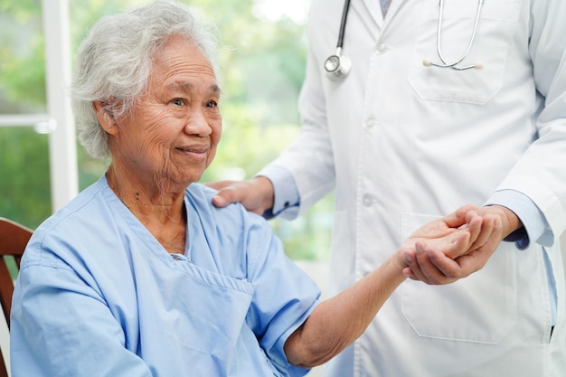 병원 에서 환자 를 돕고 돌보는 아시아인 노인 여자 의 손 을 잡은 의사