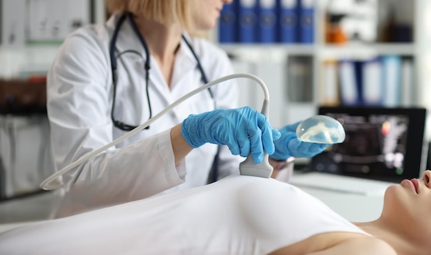 Photo doctor holding implant and doing ultrasound examination of woman breasts closeup