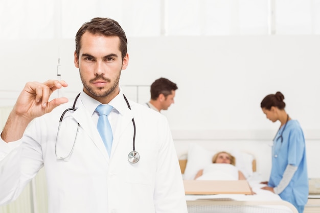 Doctor holding injection with colleagues and patient behind