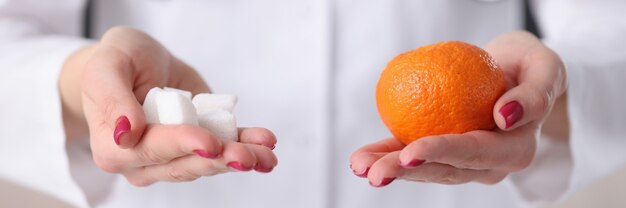 彼の手のクローズアップでオレンジと角砂糖を保持している医師。糖尿病の予防の概念