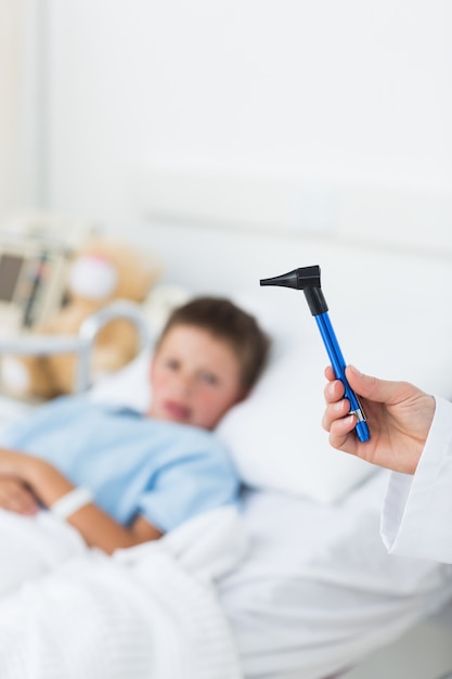 Doctor holding otoscope with boy in hospital