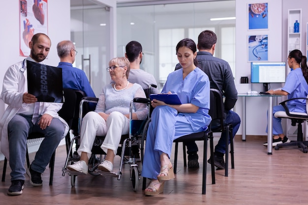 Medico che tiene i raggi x del paziente che spiegano la diagnosi all'infermiera e alla donna disabile