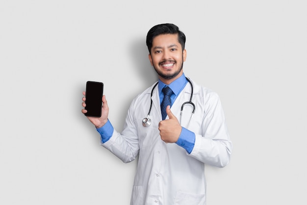 Photo doctor holding phone showing thumb up isolated. pakistani man doctor technology medicine at home. phone clear screen.